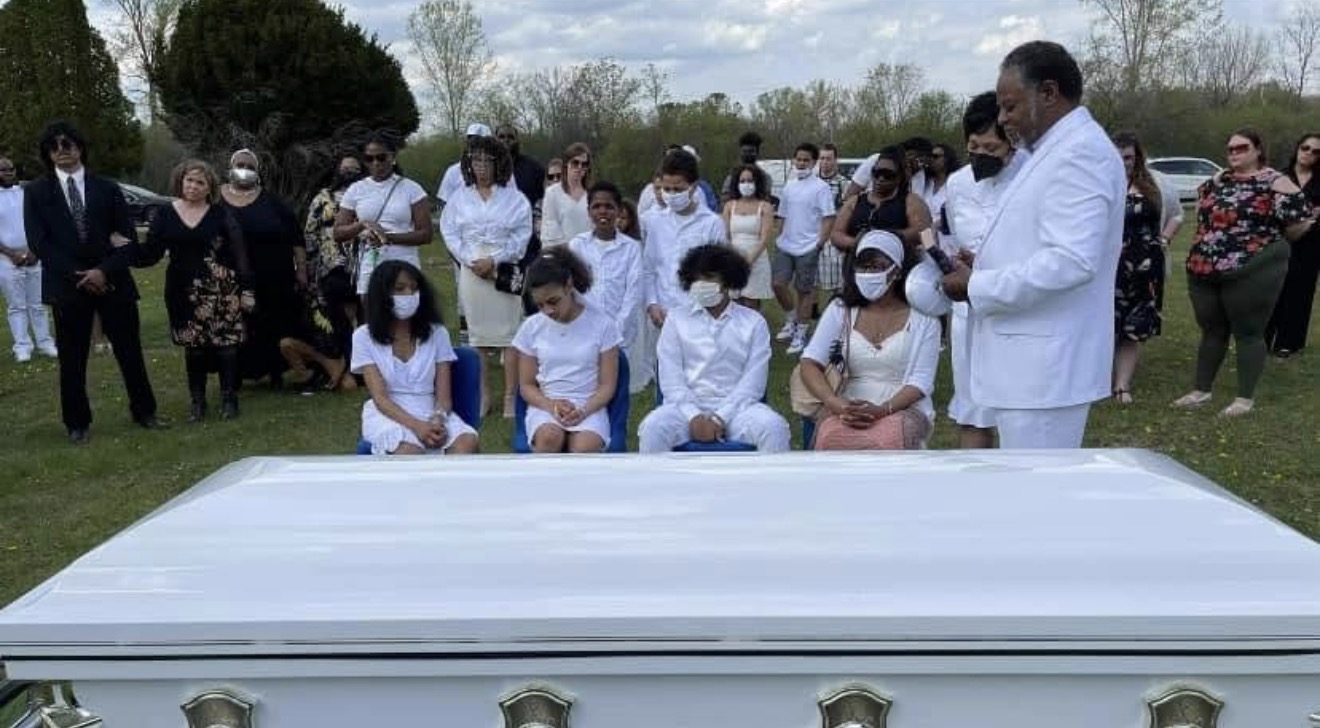 Family in white seated and standing around Jerome's white casket at the graveside service
