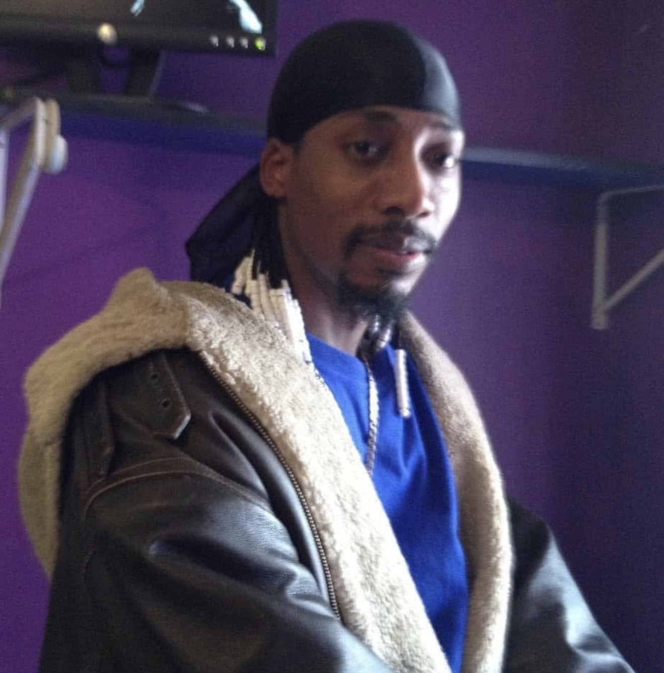 Jerome in a shearling collar leather jacket and blue shirt, looking toward the camera